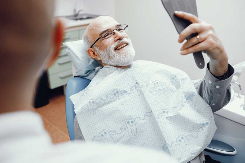 Elderly male patient admiring his smile in a handheld mirror