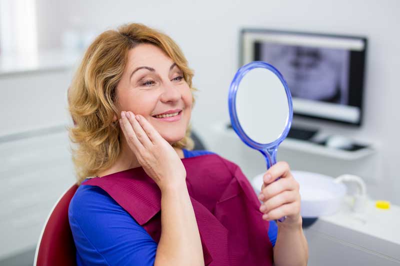 Middle-aged female patient admiring her smile in a handheld mirror